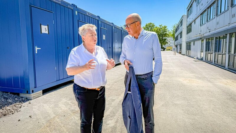 Bürgermeisterin Ulrike Mohrs im Gespräch mit Thomas Brahm. Im Hintergrund sind links die bestehenden Wohncontainer zu sehen, rechts ein neu errichtetes, modernes Wohnmodul.