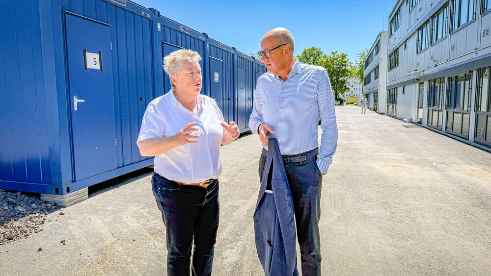 Bürgermeisterin Ulrike Mohrs im Gespräch mit Thomas Brahm. Im Hintergrund sind links die bestehenden Wohncontainer zu sehen, rechts ein neu errichtetes, modernes Wohnmodul.