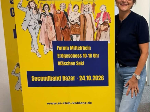 Regina Immes, Clubpräsidentin von Soroptimist International Club Koblenz/Rhein vor Werbebanner des Seconhand Bazars